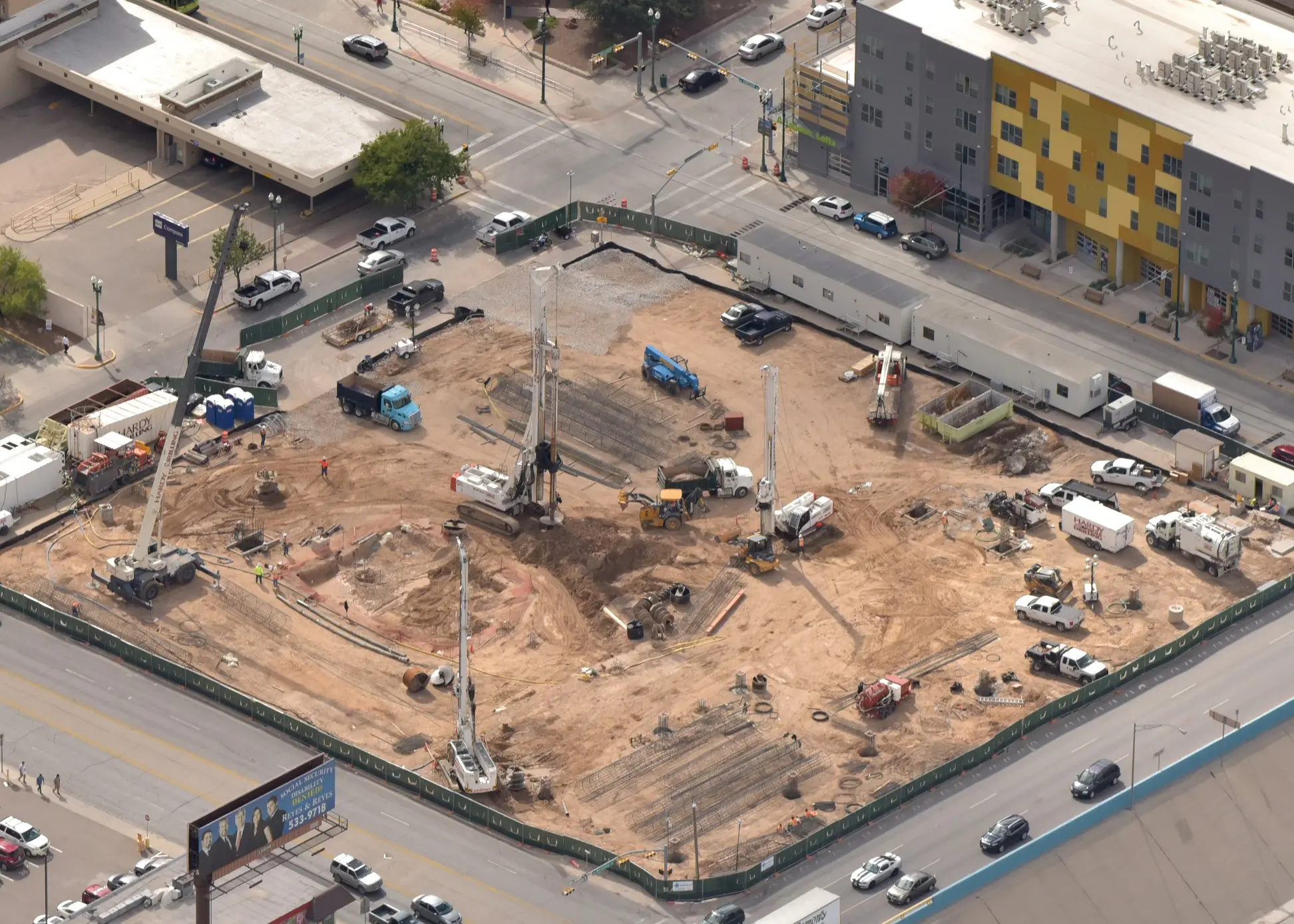 A construction site at an urban intersection with heavy machinery and workers.